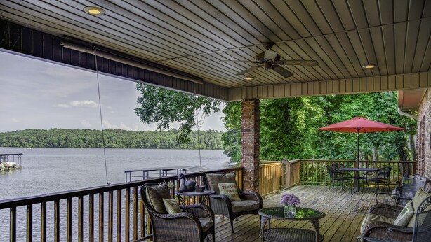 A covered deck with wicker furniture, a red umbrella, and a view of a lake. - Centrally Located Lake House with a Secluded Feel Boat Slip Included (HOT SPRINGS NATIONAL PARK)