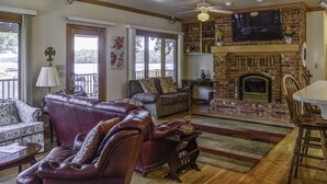 A spacious living room with a fireplace, leather sofas, a television, and a view of the outdoors. - Centrally Located Lake House with a Secluded Feel Boat Slip Included (HOT SPRINGS NATIONAL PARK)