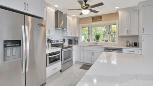 A modern kitchen with stainless steel appliances, white cabinetry, a large island, and a ceiling fan.