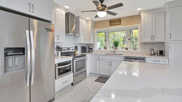 Una cocina moderna con electrodomésticos de acero inoxidable, armarios blancos, una isla grande y un ventilador de techo.