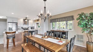Una cocina amplia con electrodomésticos modernos, un comedor con mesa de madera y un ventanal con vista a árboles.