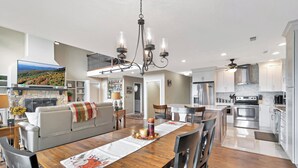 A modern kitchen with stainless steel appliances, a dining area with a wooden table and chairs, and a cozy living room with a fireplace.
