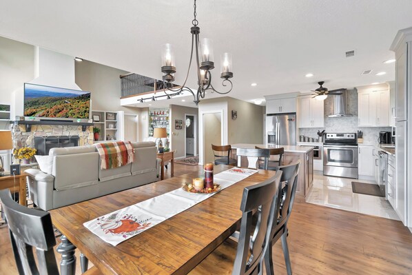 A modern kitchen with stainless steel appliances, a dining area with a wooden table and chairs, and a cozy living room with a fireplace.