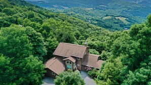 A house surrounded by dense forest with a view of rolling hills in the background.