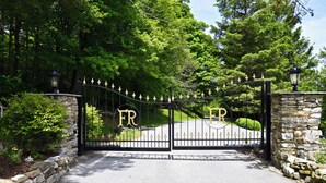 A gated entrance with a stone wall and a paved driveway leading to a well-maintained lawn.