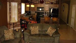 A cozy living room with a sofa and armchair, a coffee table with candles, and a kitchen area with a microwave and stove. - Single Level! 3B 2B Johnson Ranch. (San Tan Valley)