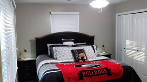 Une chambre à coucher comprenant un lit, une table de chevet, une lampe, une fenêtre avec des stores et une porte.