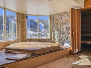 Relax in a serene room with a large bed against a stone wall, offering breathtaking views of snow-covered mountains through a large window.