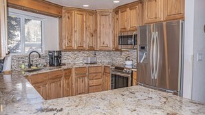A kitchen with wooden cabinets, a stainless steel refrigerator, a microwave, and granite countertops. - Spacious Luxury Condo Private Hot Tub and Sanua in Unit 1000' to ski lift (Keystone)