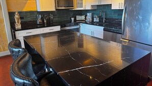 A kitchen with a large island, white cabinets, and stainless steel appliances. - Artistic Top-Floor Tropical Penthouse – Steps to Maui’s Best Beach (Kihei)