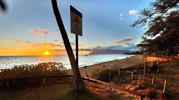 A sunset view over a beach with a sign warning of strong currents. - Artistic Top-Floor Tropical Penthouse – Steps to Maui’s Best Beach (Kihei)