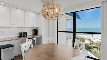 Una cocina moderna con armarios blancos, una mesa redonda de madera y un amplio ventanal con vistas a la playa.