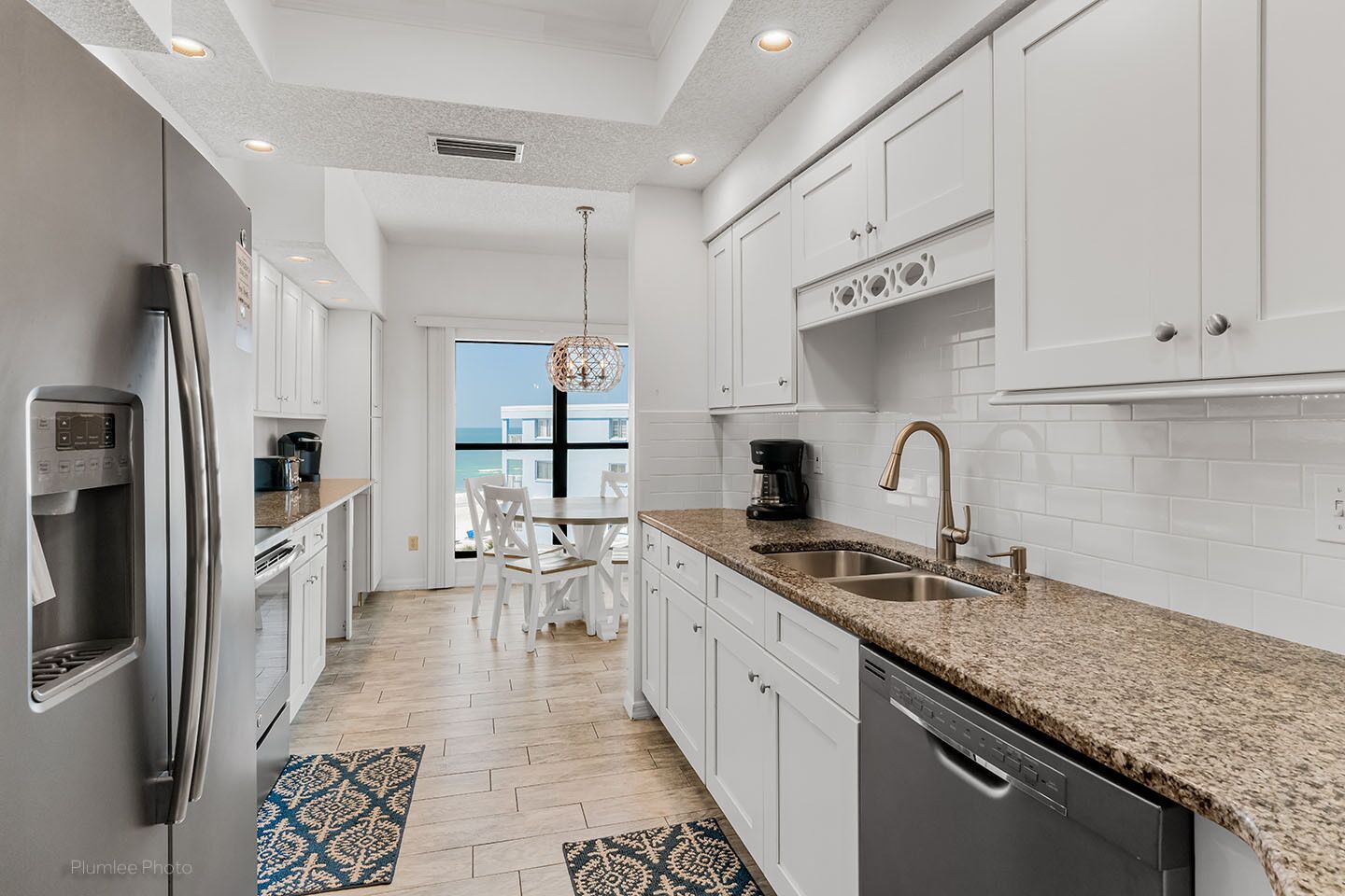 Una cocina moderna con armarios blancos, encimeras de granito y electrodomésticos de acero inoxidable, con vistas al exterior.