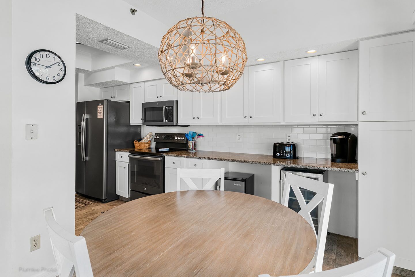A modern kitchen with white cabinets, stainless steel appliances, a round wooden dining table, and a unique woven light fixture.
