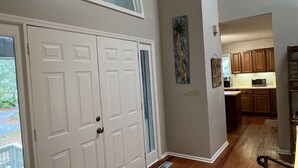 A hallway with double doors, a kitchen area with wooden cabinets, a microwave, and a coffee maker. - Precious Island Cottage (Fripp Island)