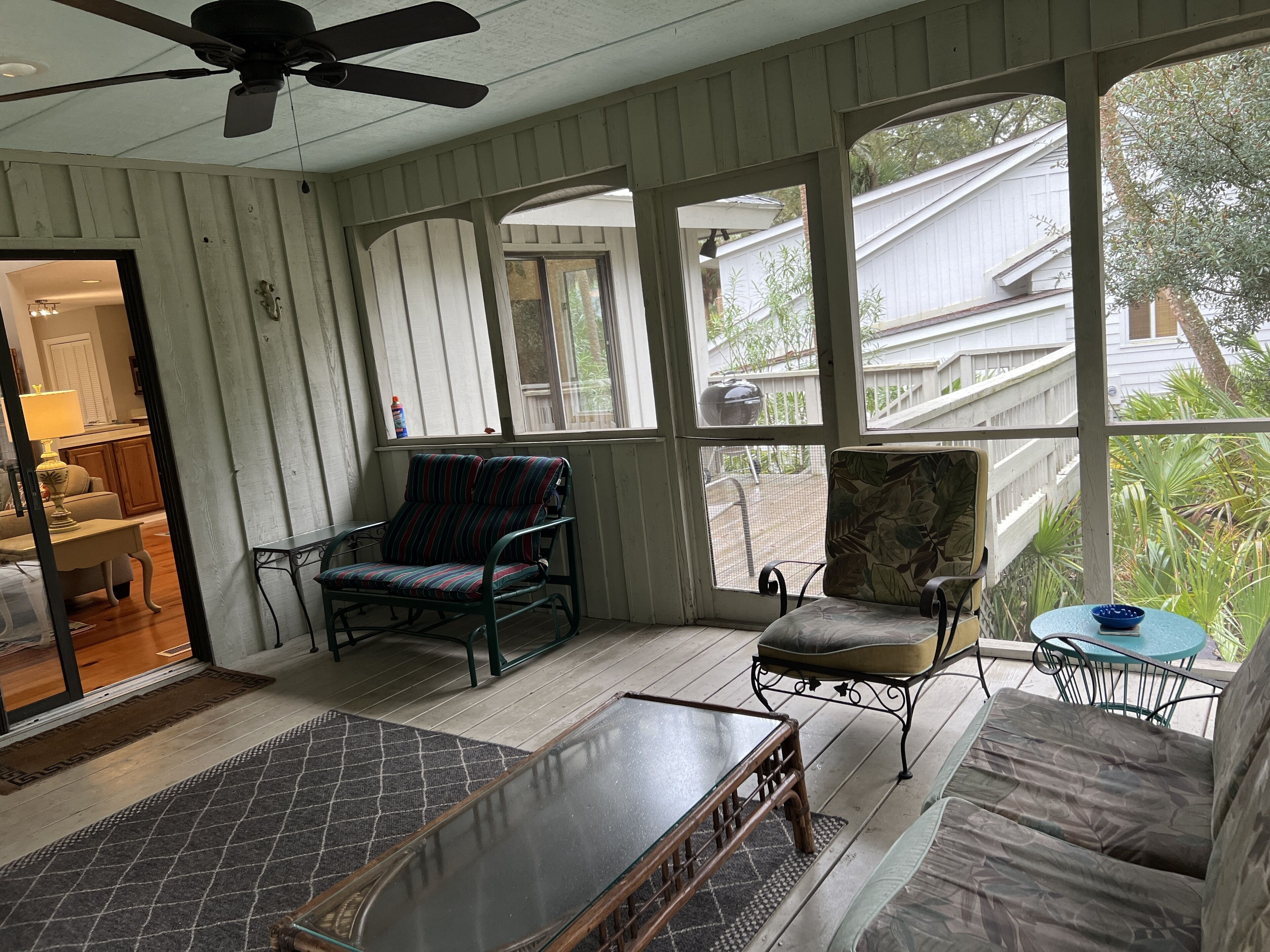 A sunroom with large windows, a ceiling fan, and a variety of seating including a sofa, chairs, and a table.