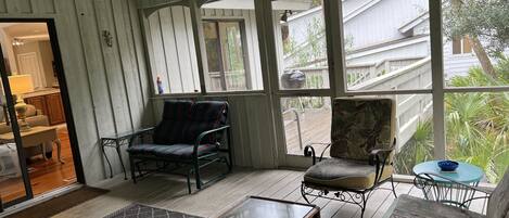 A sunroom with large windows, a ceiling fan, and a variety of seating including a sofa, chairs, and a table.