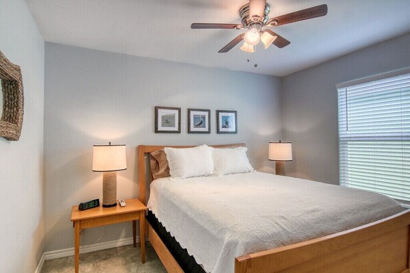 A bedroom with a bed, two bedside tables with lamps, a ceiling fan, and three framed pictures on the wall.