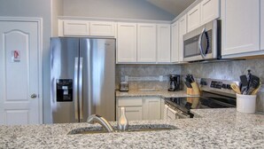 Una cocina con gabinetes blancos, electrodomésticos de acero inoxidable, encimeras de granito y horno empotrado.