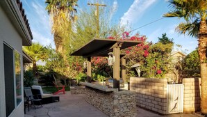 Un patio trasero con piscina, zona de barbacoa y terraza con sillas.
