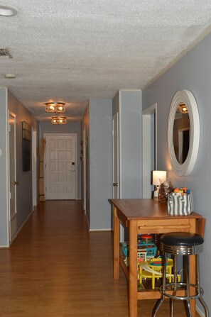 A hallway with a wooden floor, a table with a lamp, a mirror, and a toy train set. - Perfect waterfront 3/2 for your family getaway (Kingsland)