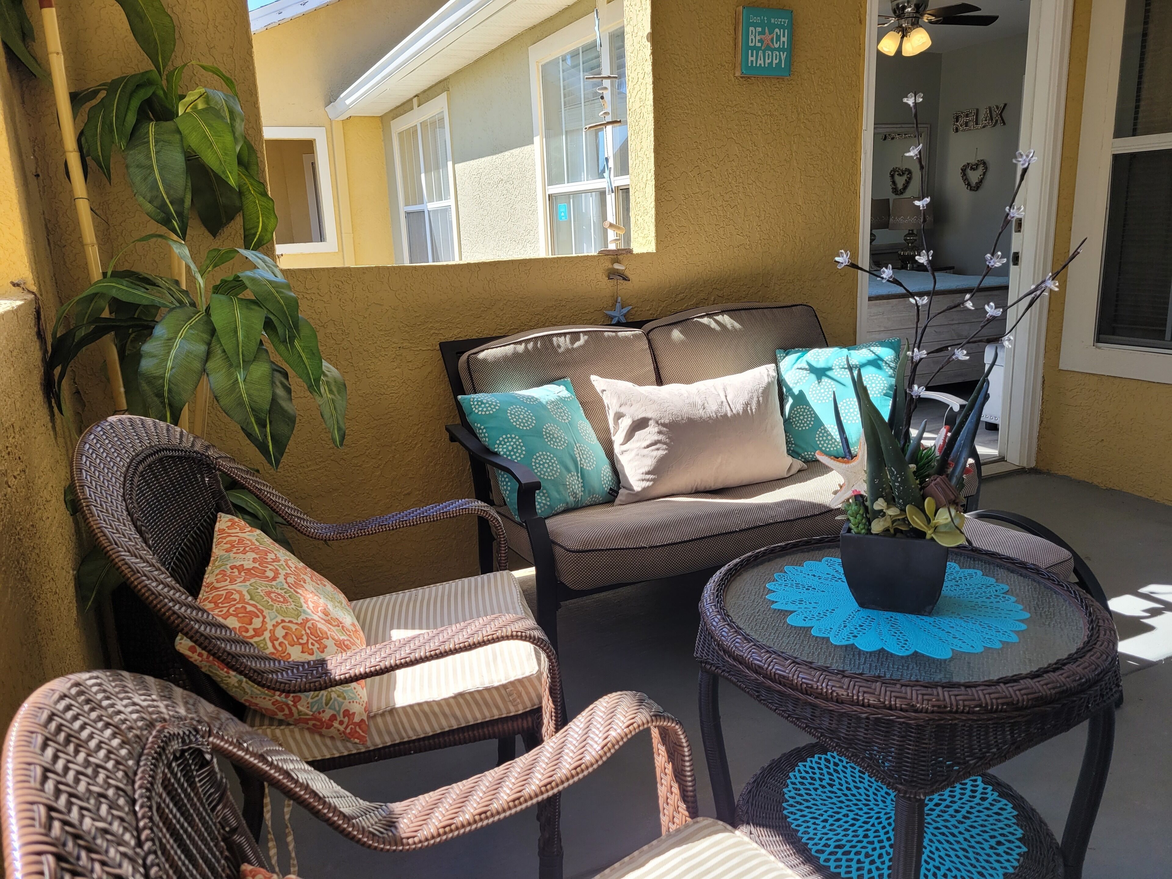 A sunlit patio with wicker furniture, a potted plant, and a ceiling fan.