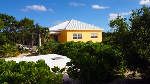 A yellow building with a white roof, surrounded by lush greenery and a clear blue sky. - Empyrean - Tangerine - Paradise in Whitby, North Caicos (Whitby)