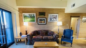 Ein Wohnzimmer mit einer Holzwand, einem blauen Sessel, einem gemusterten Sofa, einem Couchtisch und einem Fernseher.