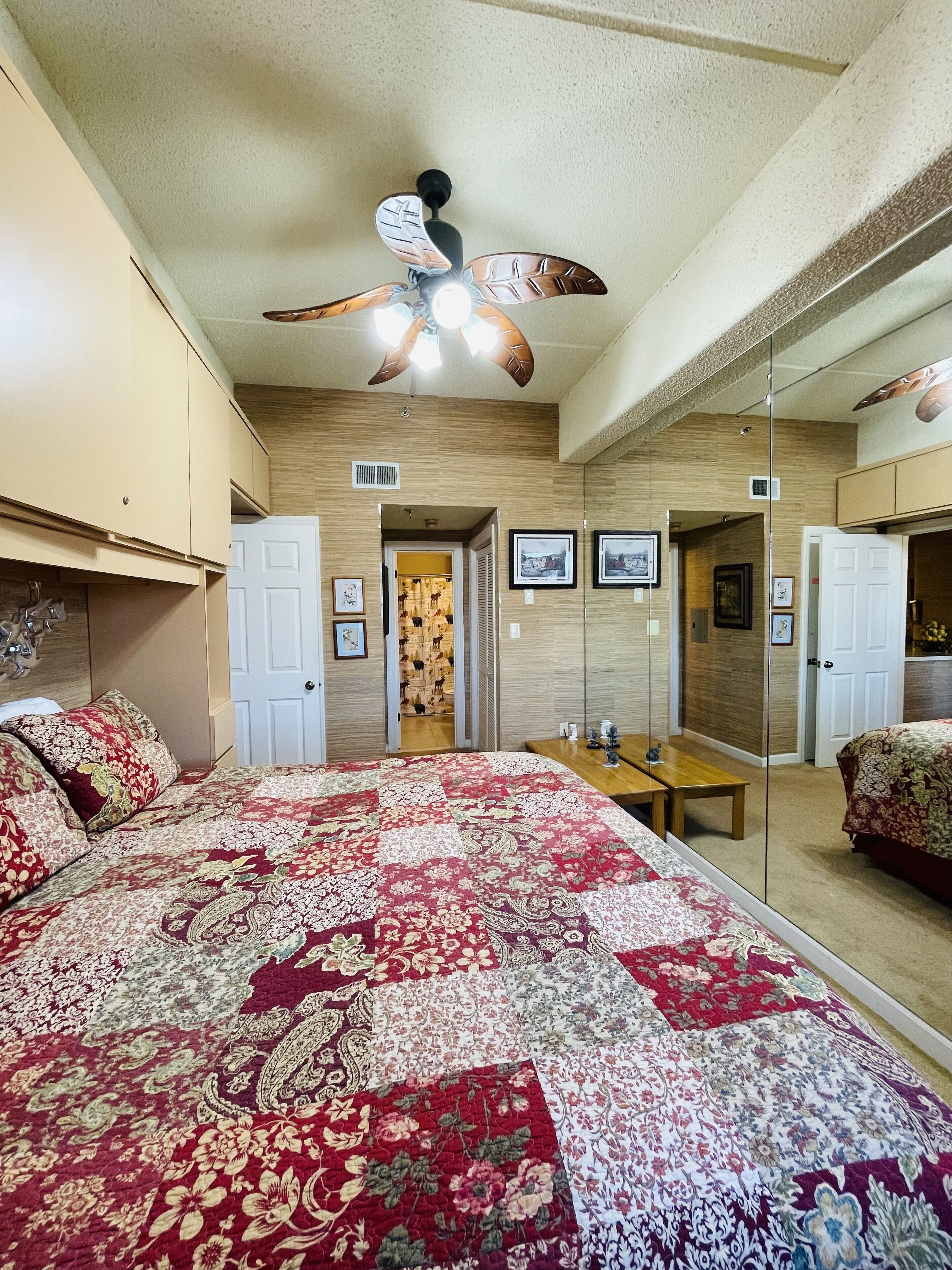 Un dormitorio con una cama grande, un ventilador de techo, un espejo y paneles de madera en las paredes.