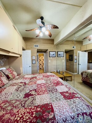 A bedroom with a large bed, a ceiling fan, a mirror, and wooden paneling on the walls. - 2B Condo w/ Panoramic Slope-Side Views (Sugar Mountain)