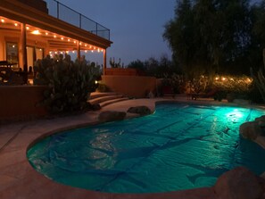 Ein Pool mit geschwungener Kante, umgeben von Steinen und einer Terrasse mit Lichterketten.