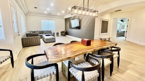 Amplia sala de estar con una mesa de comedor de madera, sillas modernas y un televisor grande montado en la pared.