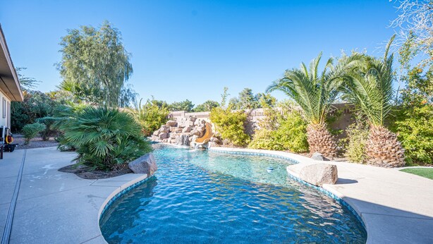 Una piscina con una cascada, rodeada de plantas y un muro de piedra.