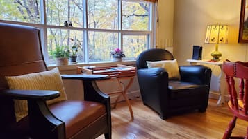Un salon chaleureux avec une grande fenêtre, une table basse en bois, un fauteuil en cuir noir et une chaise rouge.