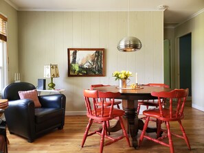 A dining area with a wooden table and red chairs, a black leather sofa, and a painting on the wall.