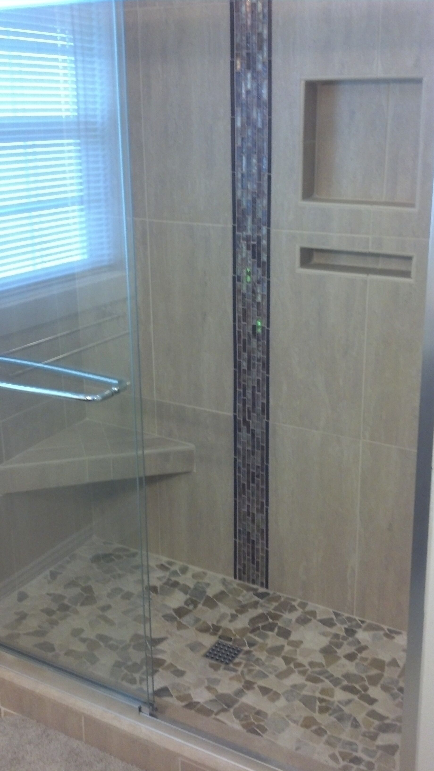 A glass-enclosed shower with a stone mosaic floor and a vertical tile accent.
