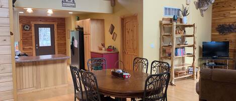 A wooden cabin interior with a dining area, kitchen, and a loft with a balcony.