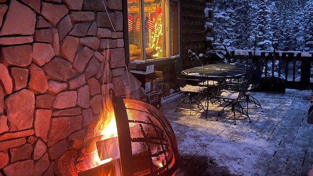 Un camino in pietra con un fuoco acceso, un patio in legno con mobili da esterno e un paesaggio innevato.