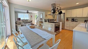 Eine moderne Küche mit weißen Schränken, ein Essbereich mit Tisch und Stühlen sowie eine separate Wohnarea mit Sofa und Fernseher.