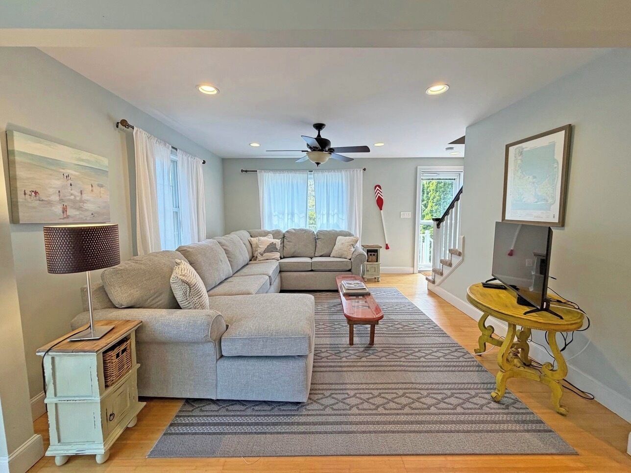 A living room with a sectional sofa, a coffee table, a TV on a stand, a lamp, and a staircase leading to another level.