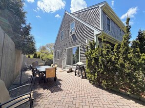 A two-story house with a patio area featuring a table and chairs, a wooden fence, and a small tree.