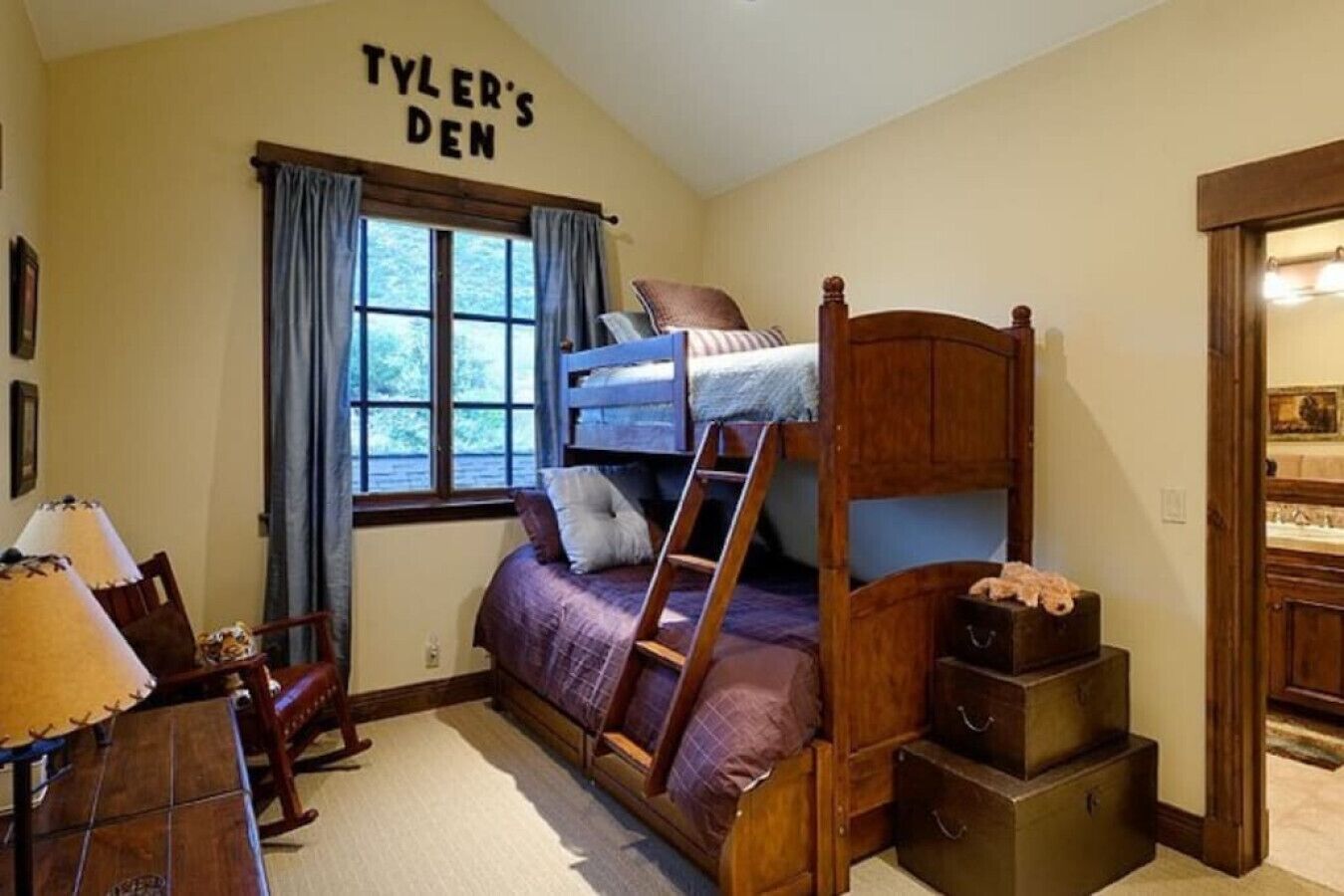 Habitación con literas, una escalera, escritorio, silla y ventana con cortinas.