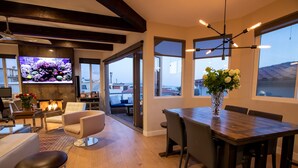 A modern living room with a fireplace, comfortable seating, a dining area, and large windows offering views of the city. - Luxury beach vacation - Ocean view bright and fun (Manhattan Beach)