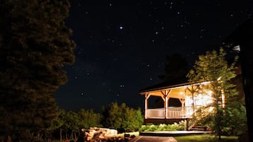 A gazebo with a wooden structure and a balcony, surrounded by trees and a clear night sky.
