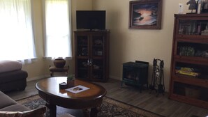 A living room with a sofa, a coffee table, a television on a stand, a fireplace, and a bookshelf. - Charming Waimea home on the Big Island- Close To Town!  (Waimea)