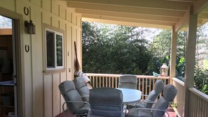 A covered patio with a round table and six chairs, a wooden deck, and a view of trees. - Charming Waimea home on the Big Island- Close To Town!  (Waimea)