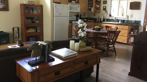 A cozy kitchen with wooden cabinets, a dining area with a table and chairs, and a bookshelf filled with books and decorative items. - Charming Waimea home on the Big Island- Close To Town!  (Waimea)