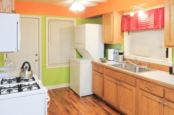 Compact kitchen with a white stove, refrigerator, and sink, featuring wooden cabinetry and a simple layout.