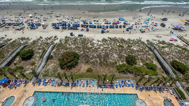 Een strandresort met een zwembad, strandparasols en ligbedden.