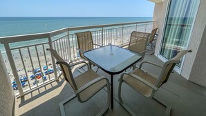 Een balkon met een tafel en stoelen met uitzicht op een strand.